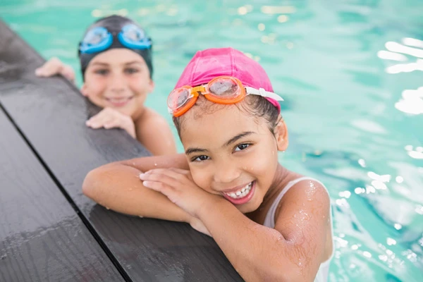 two girls in swimming caps leaning over pool ege.
