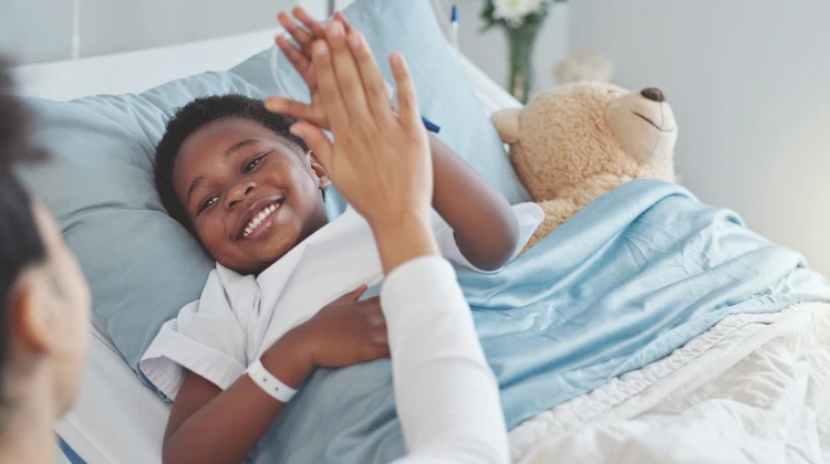 boy in hospital bed giving high five to caregiver.