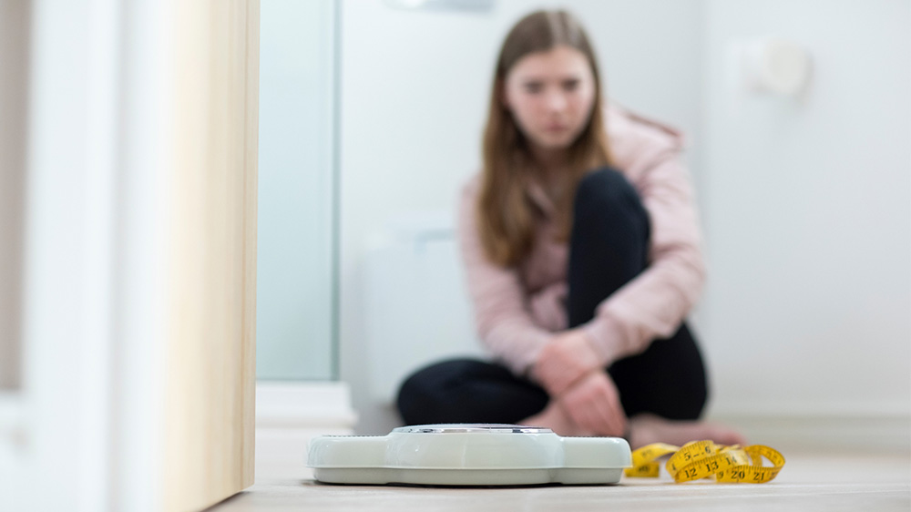 teenage girl wearily looking at a scale.