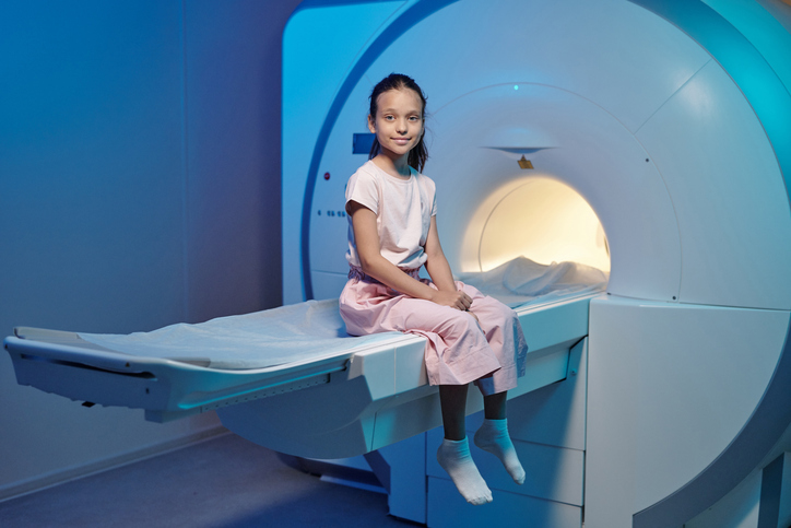 girl sitting on tray of MRI machine waiting.