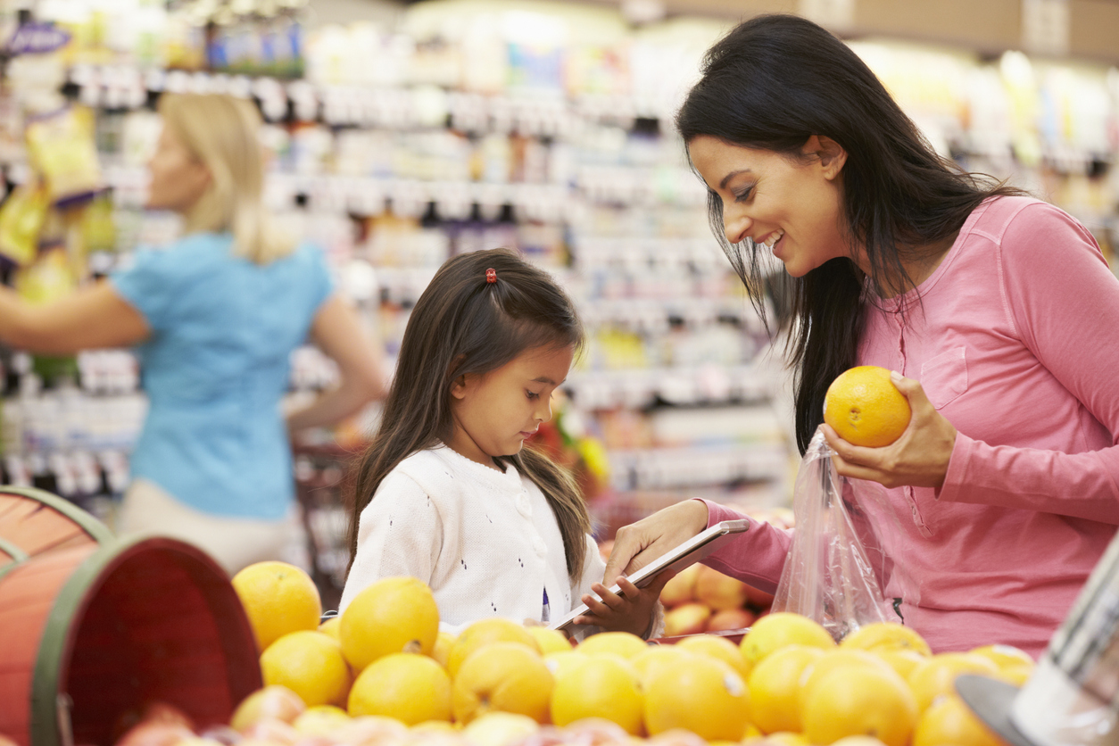 Mom shopping with daughter for oranges at grocery store.