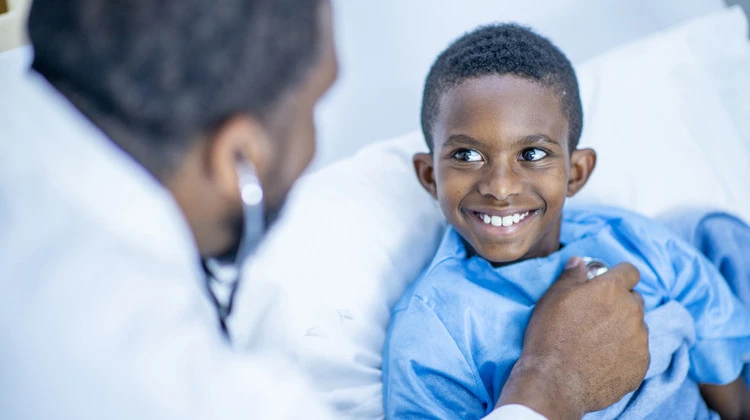 hospitalized boy smiles as doctor checks his heartbeat.