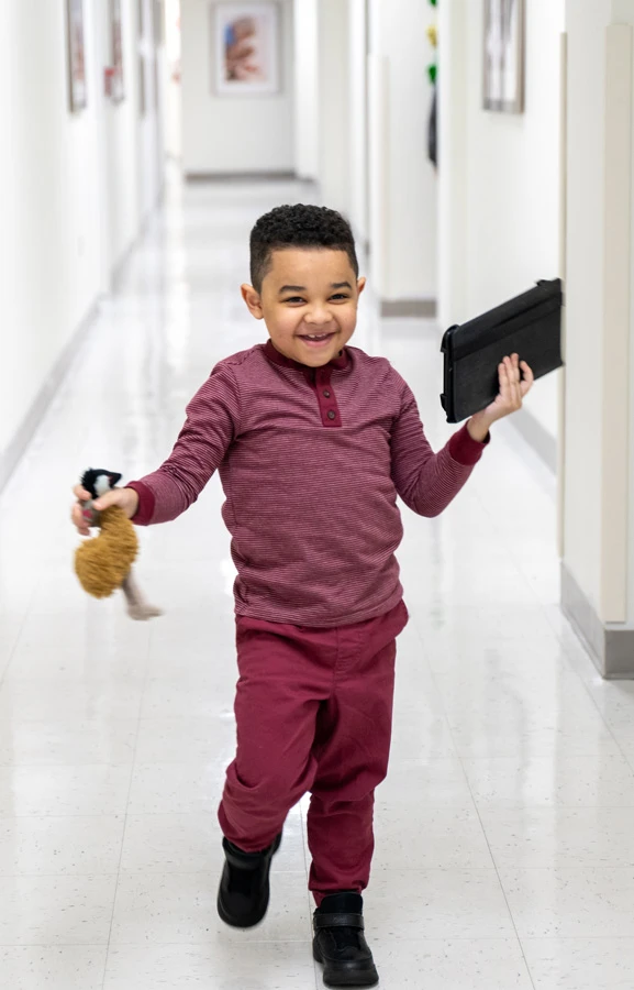 Ka'lee running down the hall holding his toy and ipad.