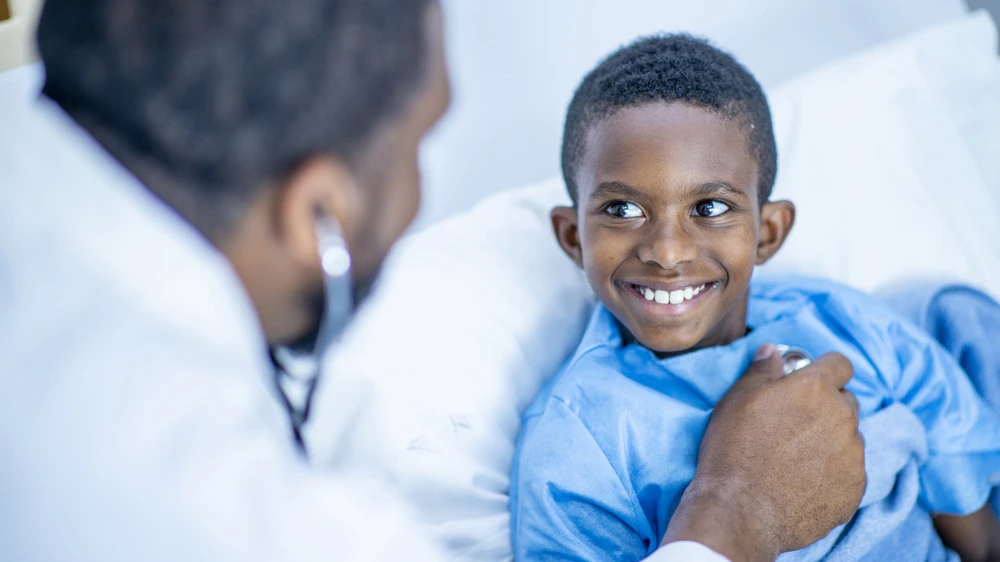 hospitalized boy smiles as doctor checks his heartbeat.