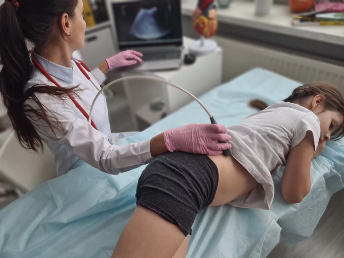 Niña sometiéndose a una ecografía de los riñones con una profesional médica.