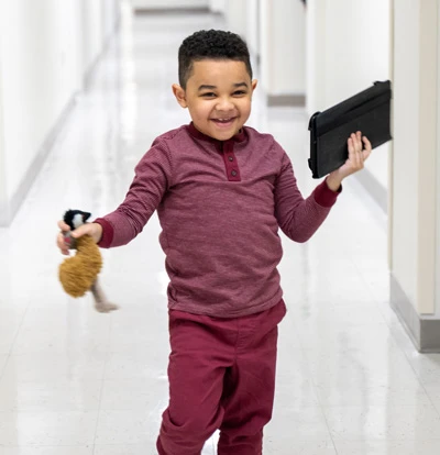 Ka'lee running down the hall holding his toy and ipad.