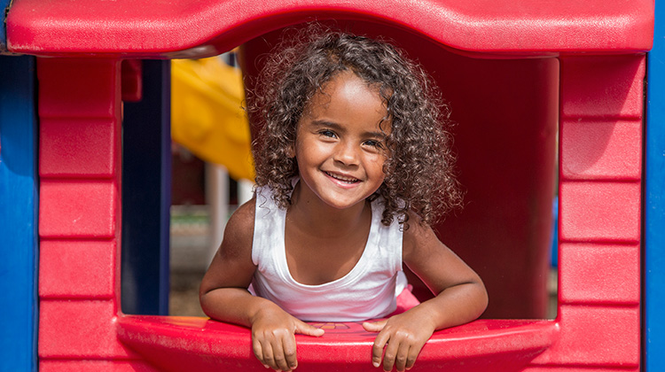 curly haired girl happily leaning out of playhouse.